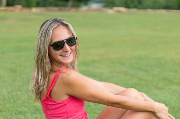 Attractive young smiling beautiful curly blonde hair slim girl fashion portrait in pink T-shirt posing looking away calm look, in background green grass meadow. Healthy woman lifestyle concept. Positive human emotions, feelings, joy. Black sunglasses. atractiva joven sonriente de pelo rubio rizado hermoso delgado retrato de moda de la muchacha en rosa camiseta posando la mirada ausente mirada calma, en pradera de hierba verde de fondo. concepto de estilo de vida saludable de la mujer. humanas emociones positivas, sentimientos, alegría. gafas de sol negro.