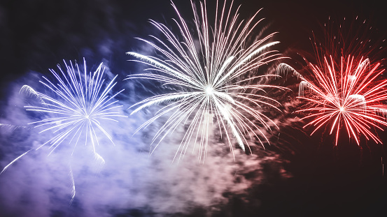 Blue, white and red like french flag colors, photography at night of beautiful large and colorful fireworks display with awe pyrotechnics and with some abstract long exposure effects. Man made light explosions during celebration event like new year or national day. This picture was taken during the Bastille Day celebrations in France on 14th of July, along Rhone river in Isere department in Auvergne-Rhone-Alpes region in Europe in Montalieu-Vercieu city.