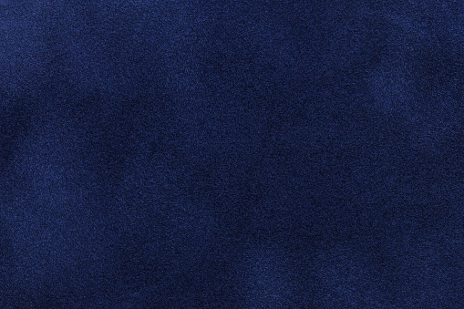 Background of dark blue suede fabric closeup. Velvet matt texture of navy blue nubuck textile.