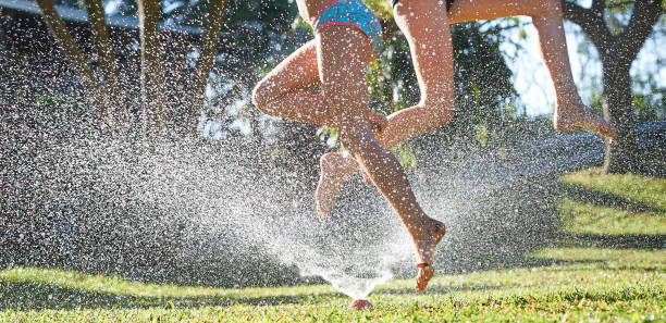 Young girls playing jumping in a garden water lawn sprinkler stock photo