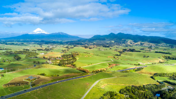 luchtfoto op een weg die loopt door landbouwgrond met mount taranaki op de achtergrond. regio taranaki, nieuw-zeeland - areal stockfoto's en -beelden