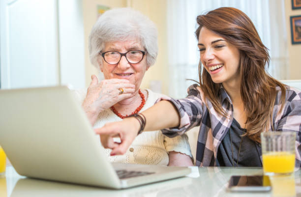 granddaughter showing her grandmother something on laptop. - wireless technology cheerful granddaughter grandmother imagens e fotografias de stock