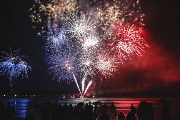 Beautiful blue white and red firework pyrotechnics show like french flag colors with unrecognizable crowd silhouettes watching stock photo