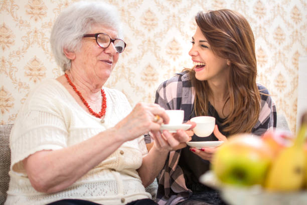 alegre nieta y su abuela junto con tazas de café en casa. - grandmother granddaughter senior adult teenager fotografías e imágenes de stock