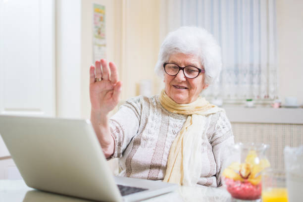 grauhaarige senior frau winkt hand vor laptop während videoanruf mit ihrer familie mitglieder. - video voip fotos stock-fotos und bilder