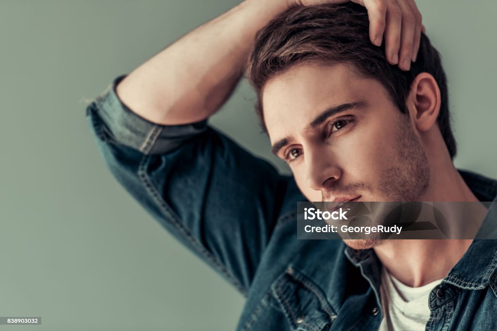 Handsome young man Portrait of handsome young man in casual clothes smoothing his hair, on gray background Adult Stock Photo