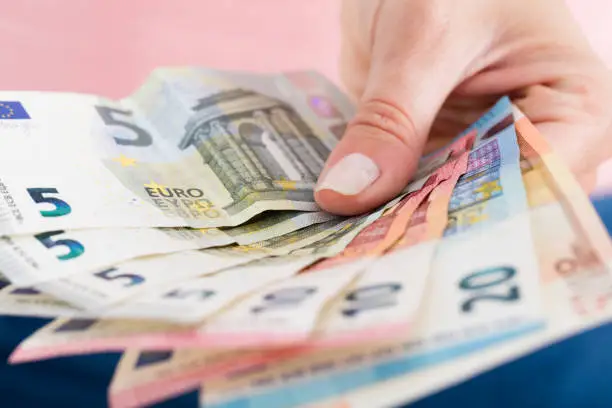 Close-up Of Person Hand Showing Fanned Euro Currency Notes On Pink Background