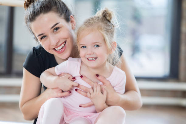 Adorable little ballerina smiles for camera with dance instructor An adorable preschool age ballerina smiles for the camera with her dance instructor.  Her instructor is behind her with her arms wrapped around her in embrace. dance studio instructor stock pictures, royalty-free photos & images