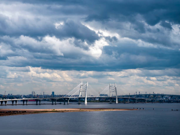 Dark clouds looming over the outskirts and port of St Petersburg, Russia, with a sudden bright shaft of sunlight illuminating the suspension bridge.