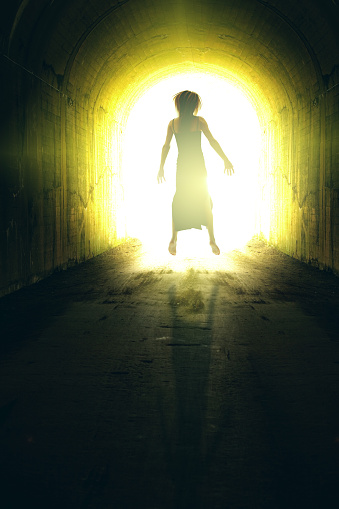 A conceptual image of a woman's body floating toward a bright light at the end of a tunnel.