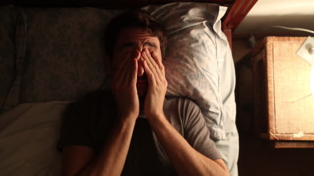 Man unable to sleep rubs his eyes and gets out of bed after having taken a nap