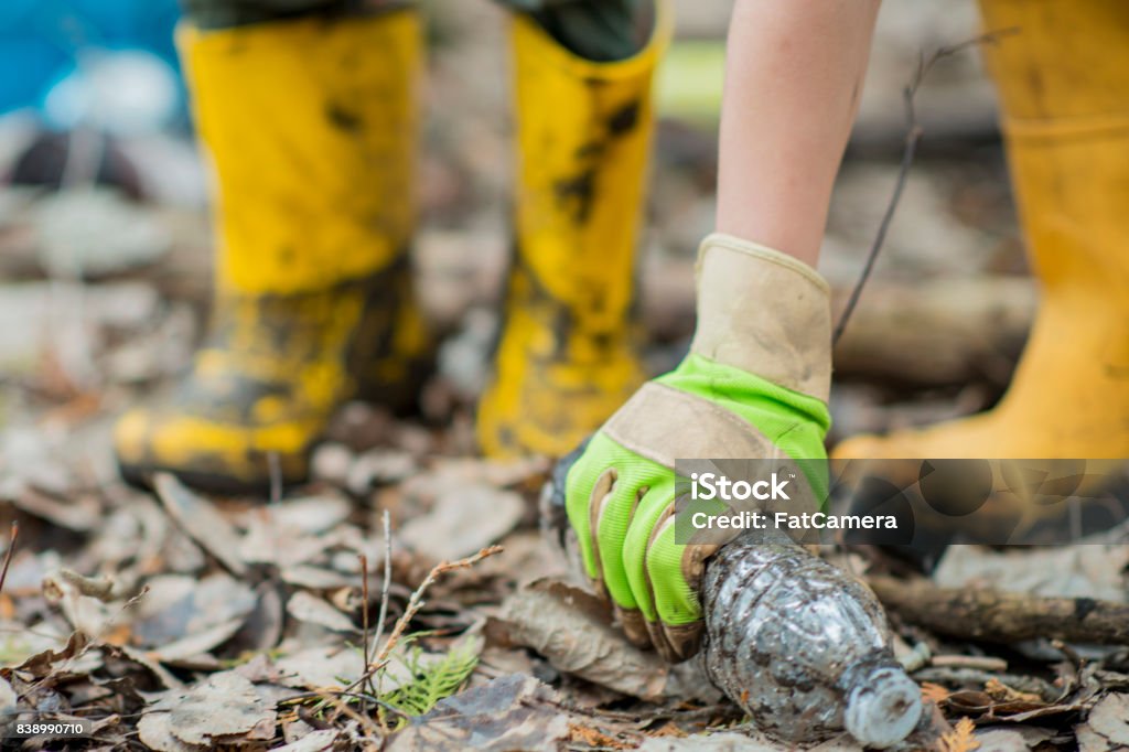 Recycling An Ethnic brother and sister are outdoors in a muddy forest. They are wearing casual clothing, rubber boots, and gloves. They are  picking up plastic bottles to recycle. Garbage Stock Photo