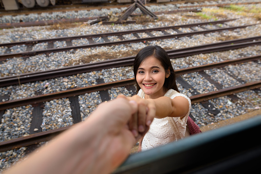 Portrait of young beautiful Asian woman holding hand of man at the railway station Hua Lamphong in Bangkok Thailand horizontal shot