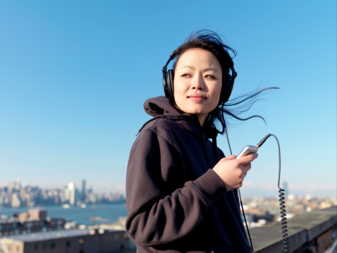 A young Asian woman listens to her headphones while smiling and looking away.