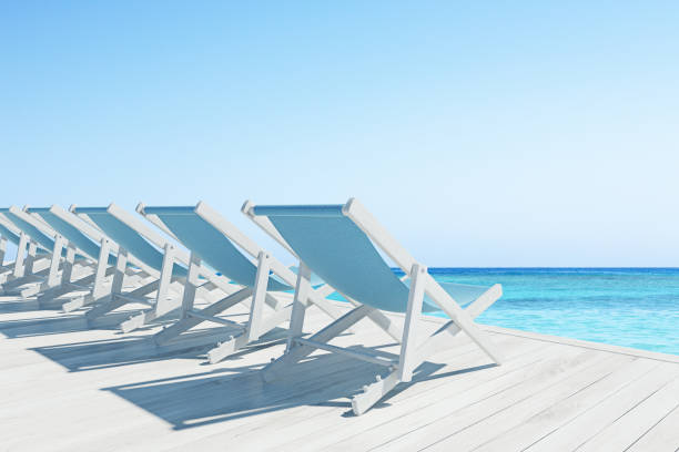 Row of blue and wooden deck chairs standing on a wooden pier near an ocean. Cloudless sky. 3d rendering mock up