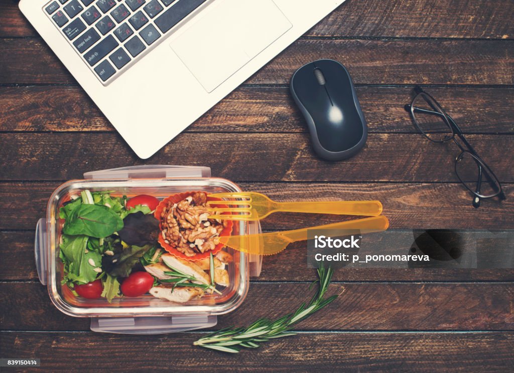 Healthy business lunch at workplace. Vegetables and fried chicken lunch box on working desk with laptop and glasses. Lunch Stock Photo