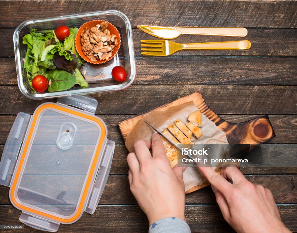 Woman preparing takeaway meal for her child. School lunch box with salad, fried chicken and nuts on rustic wooden background. Healthy eating habits concept. Lunch Stock Photo