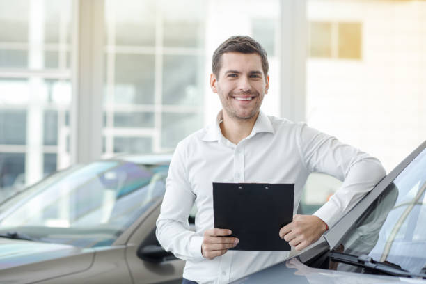 Young Man in a Car Rental Service Transportation Concept Young man in a car rental service holding contract reduction looking at camera finance business stock pictures, royalty-free photos & images