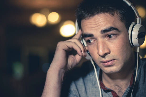 The image displays a sad teenage boy listening to music and viewing something upsetting on his cellphone. He is wearing a backpack, hoodie and headphones.