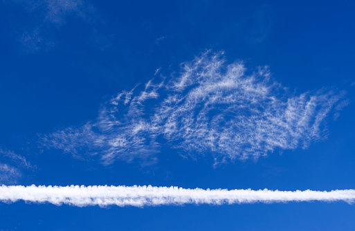 Cloudscape with a large contrail in front of higher thin and wispy cirrus clouds over Eastern Thuringia in September