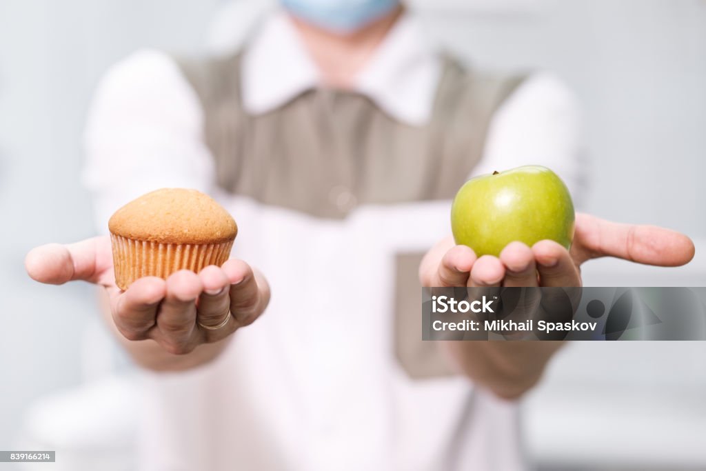 Doctor dentist man speaks about healthy nutrition and dental health Doctor a dentist a man holds a green apple and a sweet cupcake and shows on the scales a choice of useful against harmful Healthy Eating Stock Photo