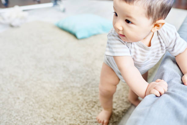 First Steps of Cute Baby Boy Full-length portrait of adorable baby boy holding on cozy sofa while learning to walk, interior of spacious living room on background first steps stock pictures, royalty-free photos & images