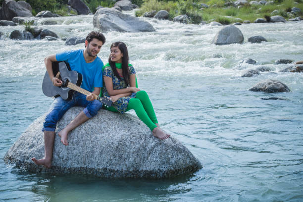 istock Young couple sitting on rock in river and playing guitar. 839175056