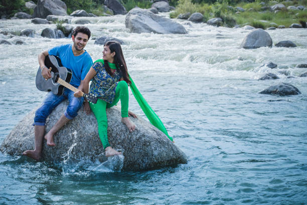 istock Young couple sitting on rock in river and playing guitar. 839175058