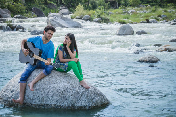 istock Young couple sitting on rock in river and playing guitar. 839175062