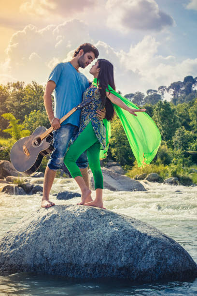 Young couple doing romance on rock in river holding guitar.