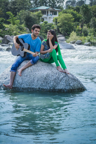istock Young couple sitting on rock in river and playing guitar. 839175074