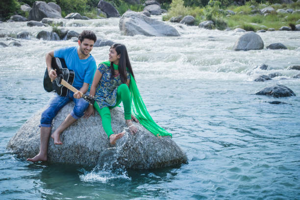istock Young couple sitting on rock in river and playing guitar. 839175080