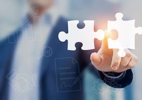 Mergers and acquisition concept with consultant touching icons of puzzle pieces representing the merging of two companies or joint venture, partnership