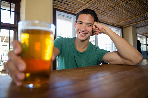 Portrait of happy man holding beer glass at counter in restaurant
