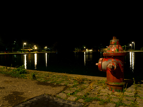 An old fire hydrant next to a lake and lights at night.
