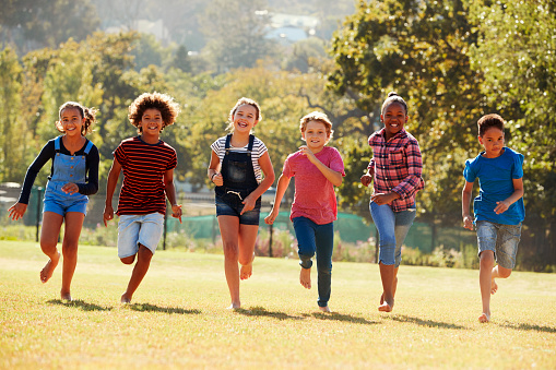 Six pre-teen friends running in a park, front view, close up