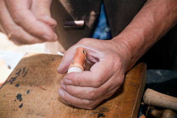 Outdoors market stall, close-up view of shoemaker's hands manufacturing toy mini leather boots, right hand moving away. Art and craft traditional festival in Lugo province, Galicia, Spain.