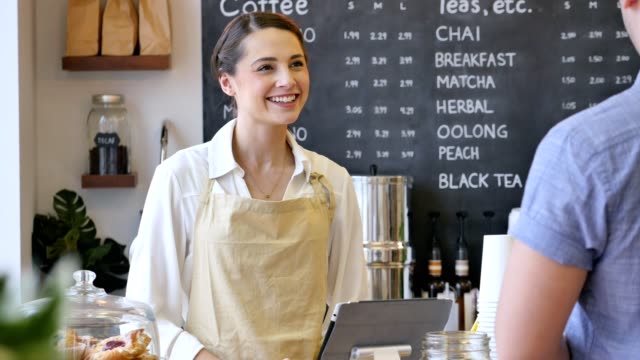 Friendly female barista helps male customer in cafe