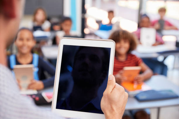 Teacher holding tablet in school class, over shoulder view