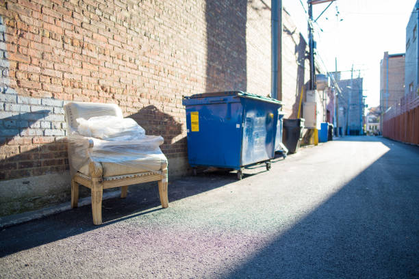 Vintage chair discarded in alley next to dumpsters, wrapped in plastic from someone's recent move. Abandoned for anyone to take for free.