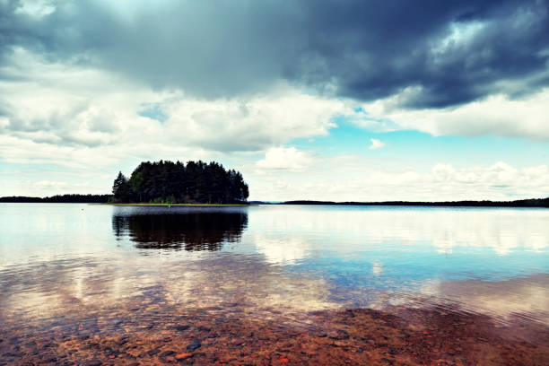 Small island reflected in the pure water of the  lake. Dramatic cloudscape.