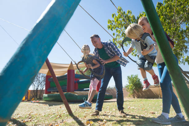 Playful parents swinging children at playground during sunny day