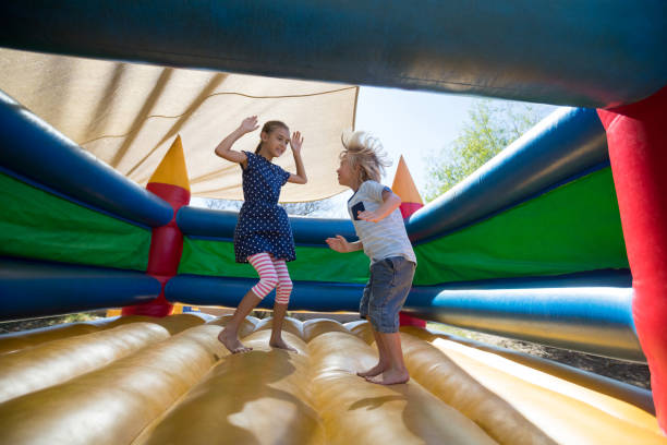 Happy siblings jumping on bouncy castle at playground Full length of happy siblings jumping on bouncy castle at playground bouncing stock pictures, royalty-free photos & images