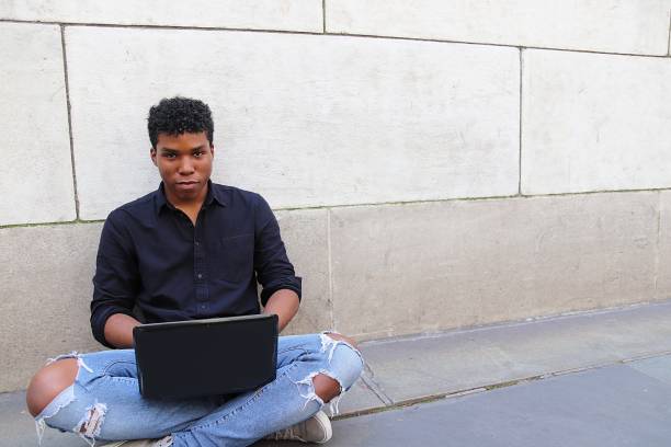 istock Young man sitting outside against concrete wall using laptop 839372358