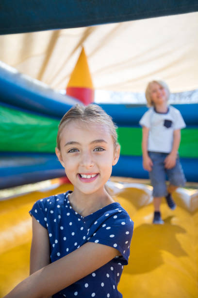 istock Girl sitting on bouncy castle while brother playing in background 839372522