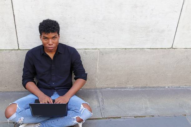 istock Young man sitting outside against concrete wall using laptop 839372966