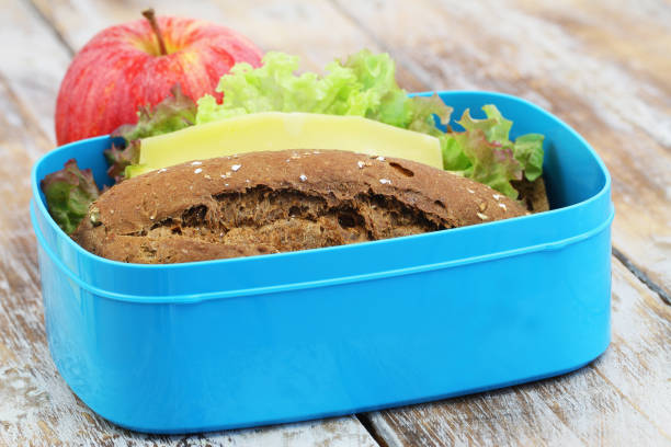 Packed lunch box containing brown cheese sandwich and red apple on rustic wooden surface