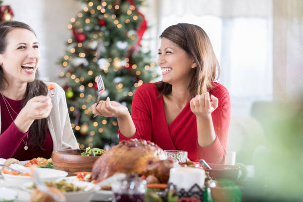 Two friends laugh together while eating Christmas dinner
