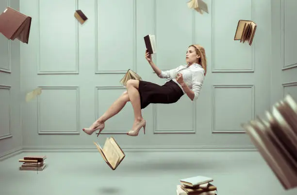 Photo of A relaxed woman levitates in a room full of flying books