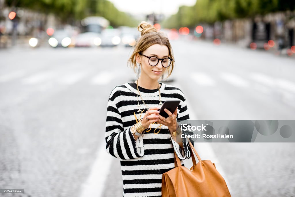 Business woman with phone on the street Young stylish woman in striped sweater using a smart phone standing outdoors on the street in Paris Women Stock Photo